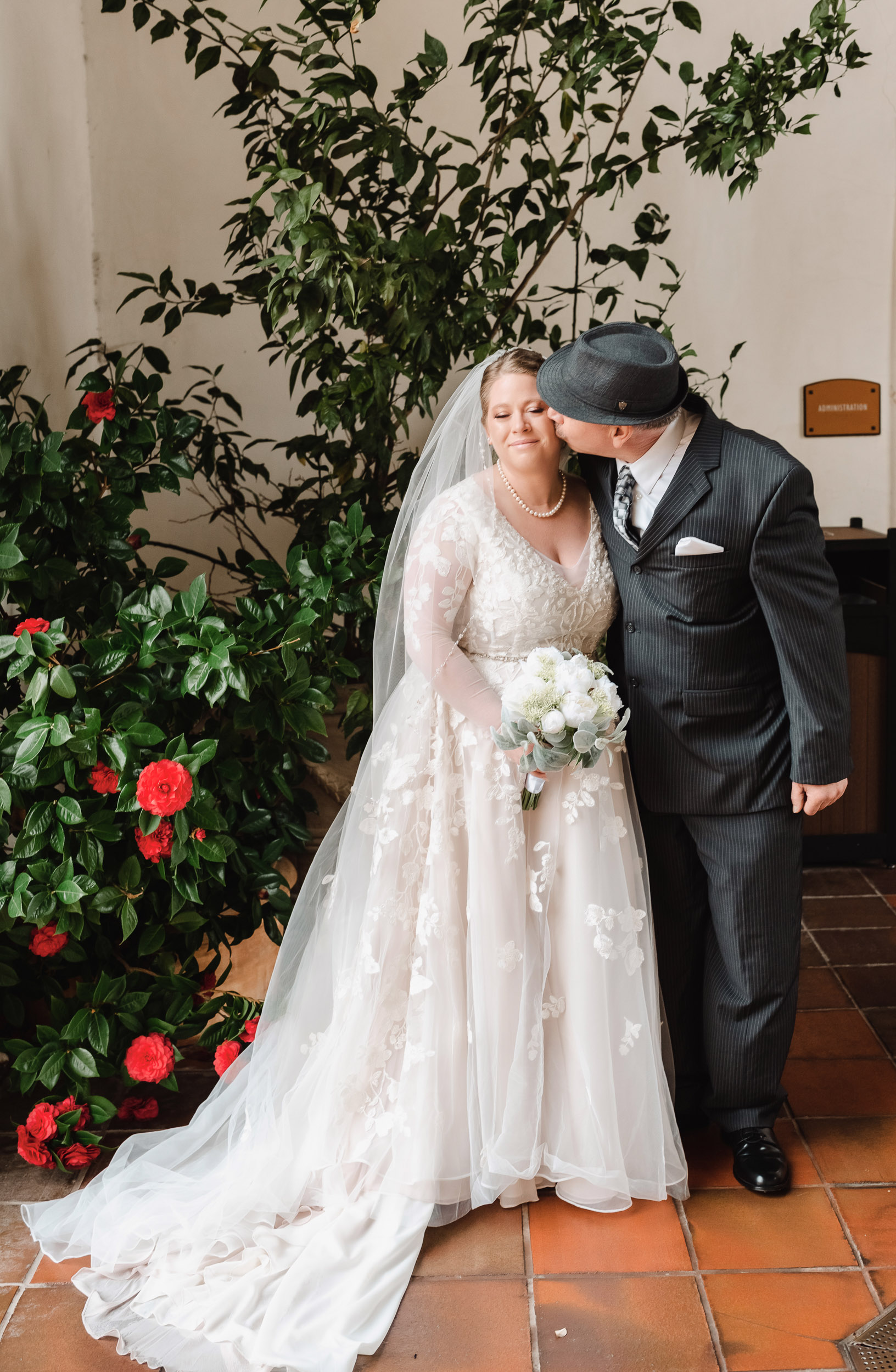 A bride and dad kissing in a courtyard.