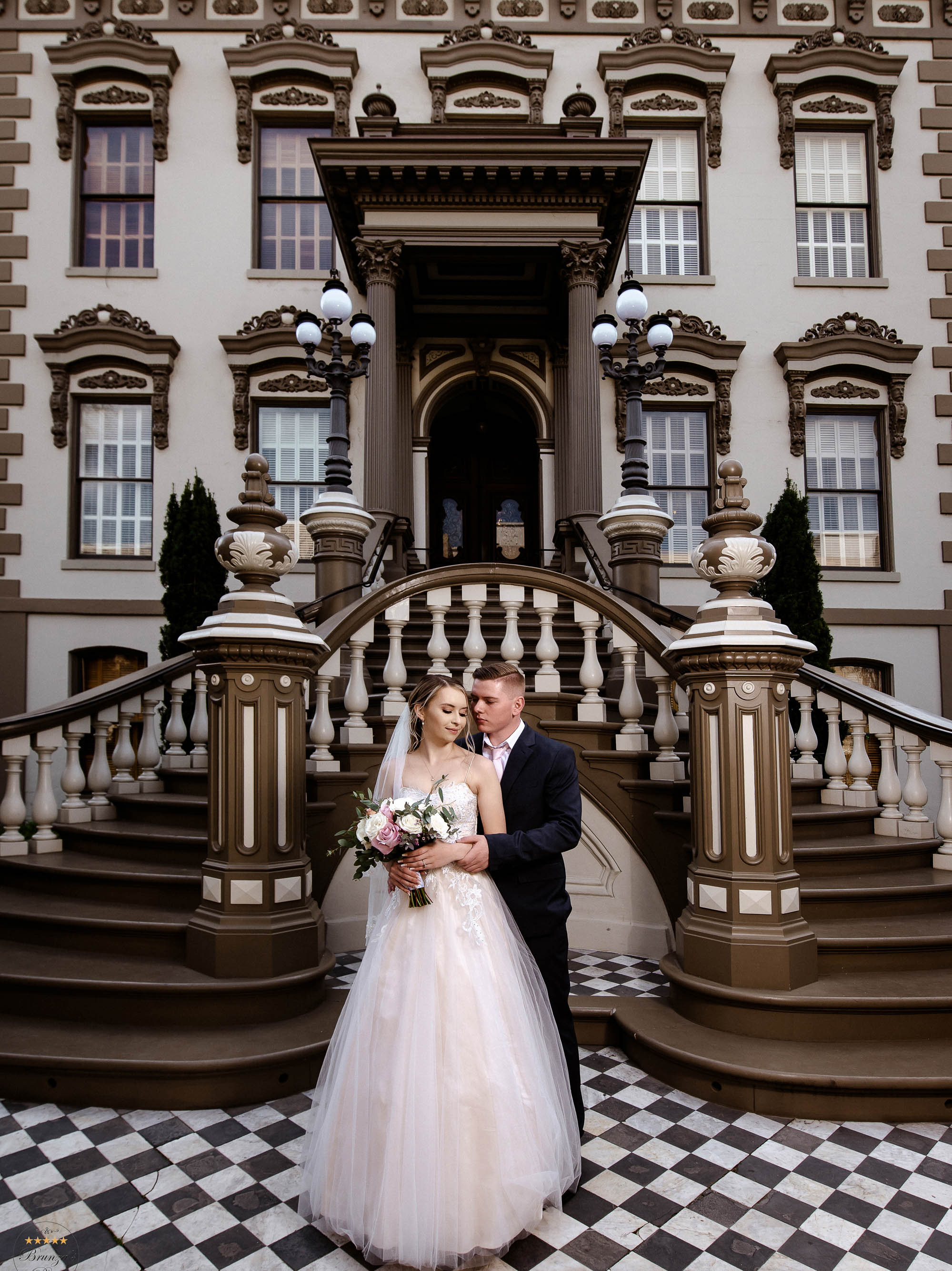 A bride and groom standing in front of an ornate mansion.
