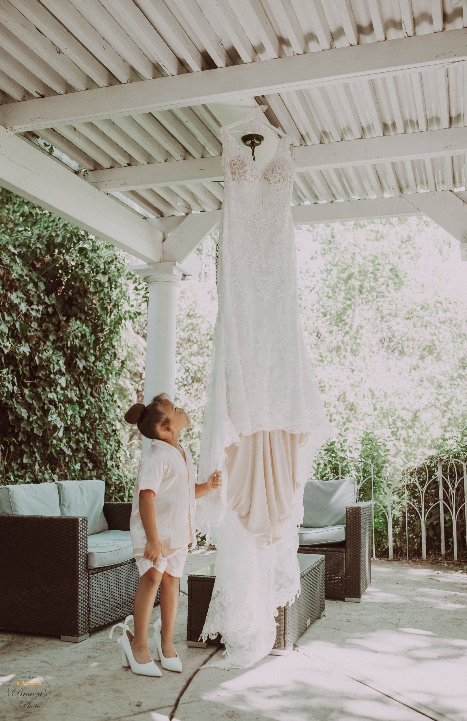 A little girl looking at a wedding dress hanging on a patio.
