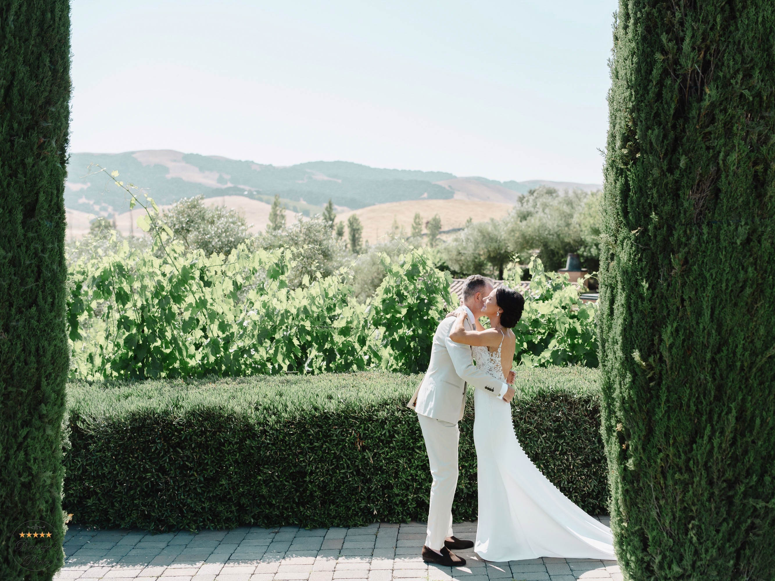 A bride and groom kiss in front of a grove of cypress trees.