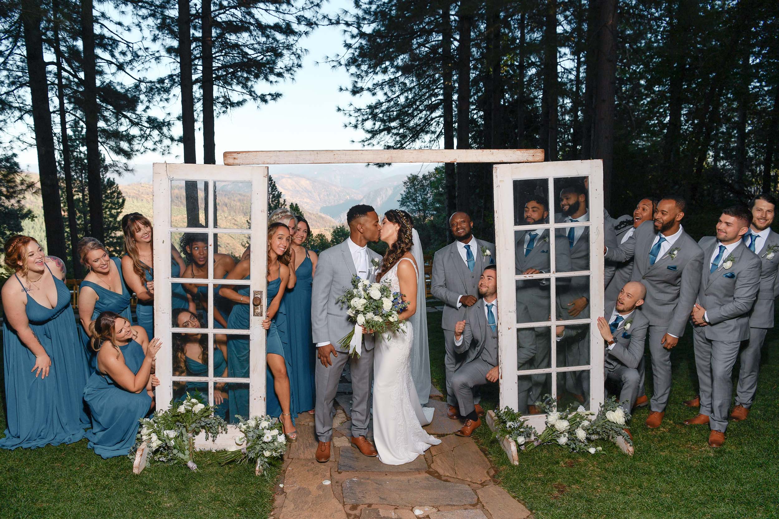 A group of bridesmaids and groomsmen pose in front of an old window.