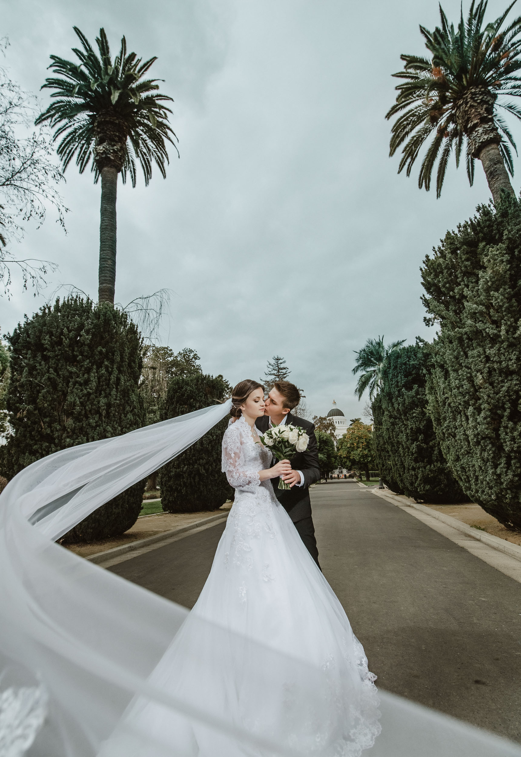 A bride and groom kissing in front of palm trees.