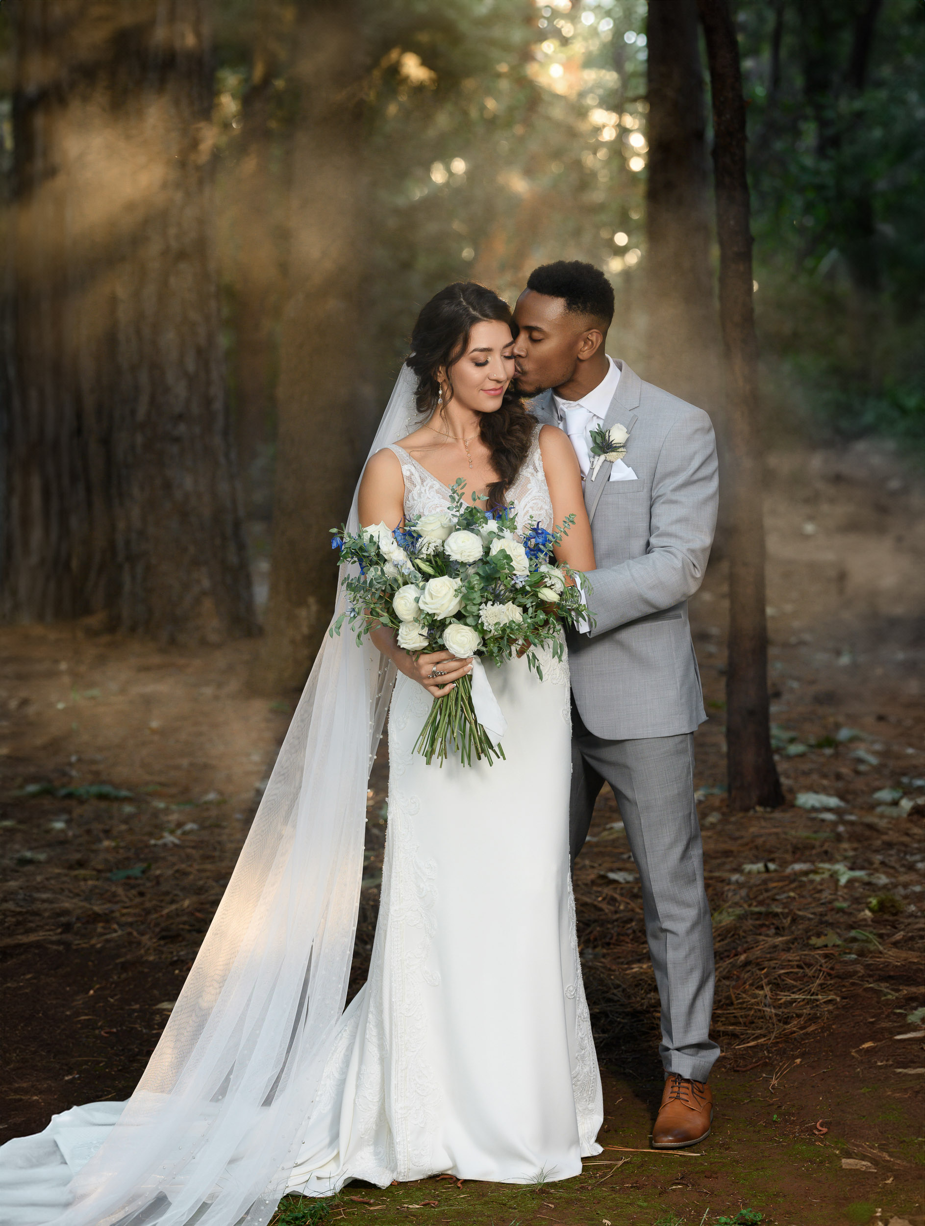 A bride and groom embracing in the woods.