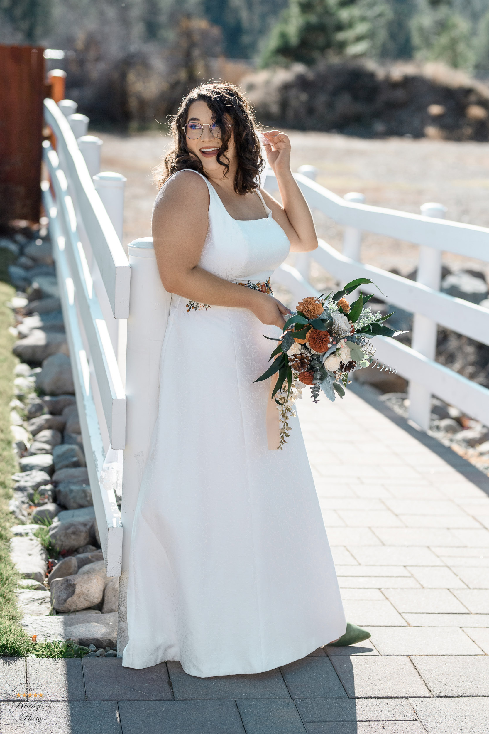 A bride in a white wedding dress standing on a wooden bridge.