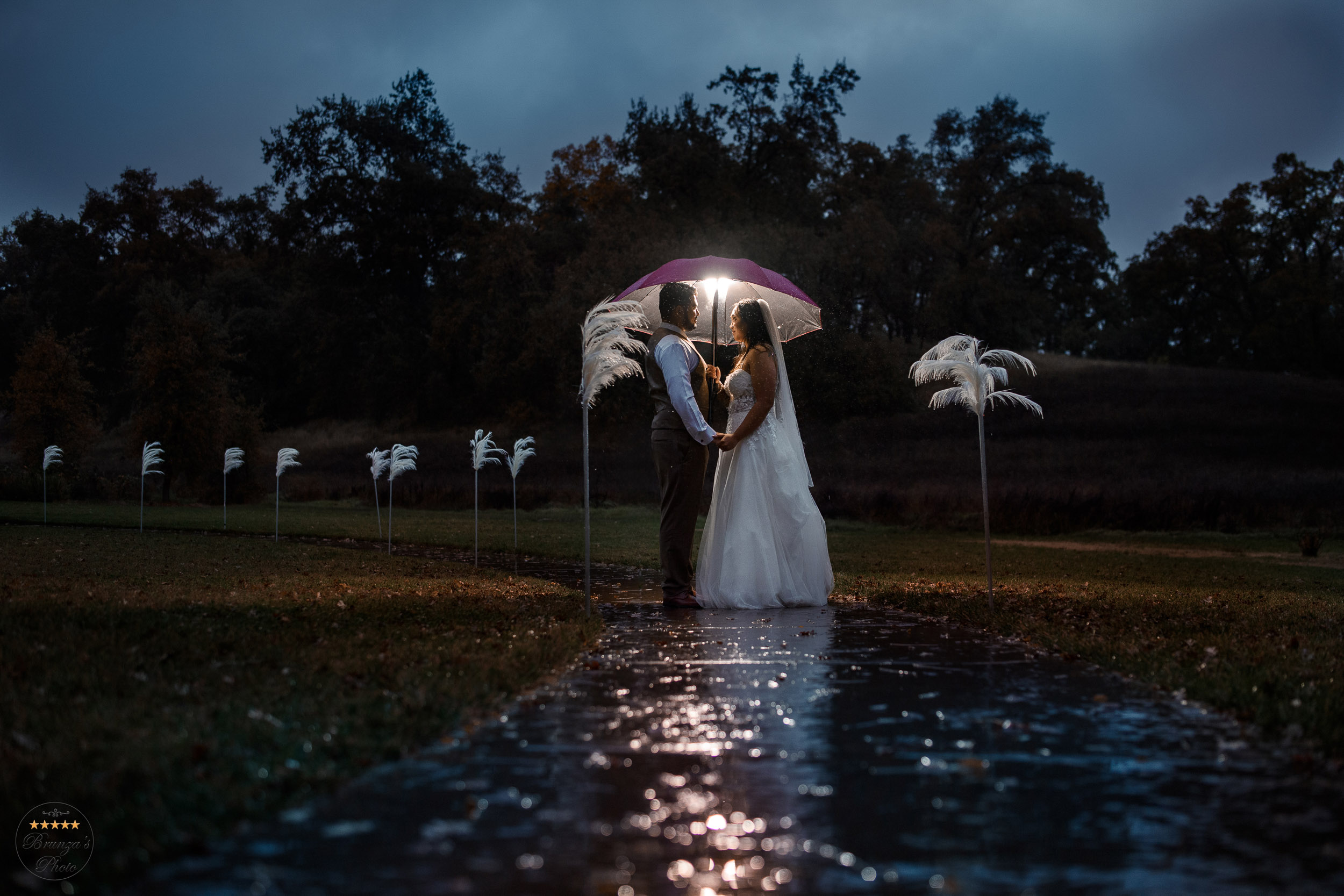 A bride and groom standing under an umbrella in the rain.