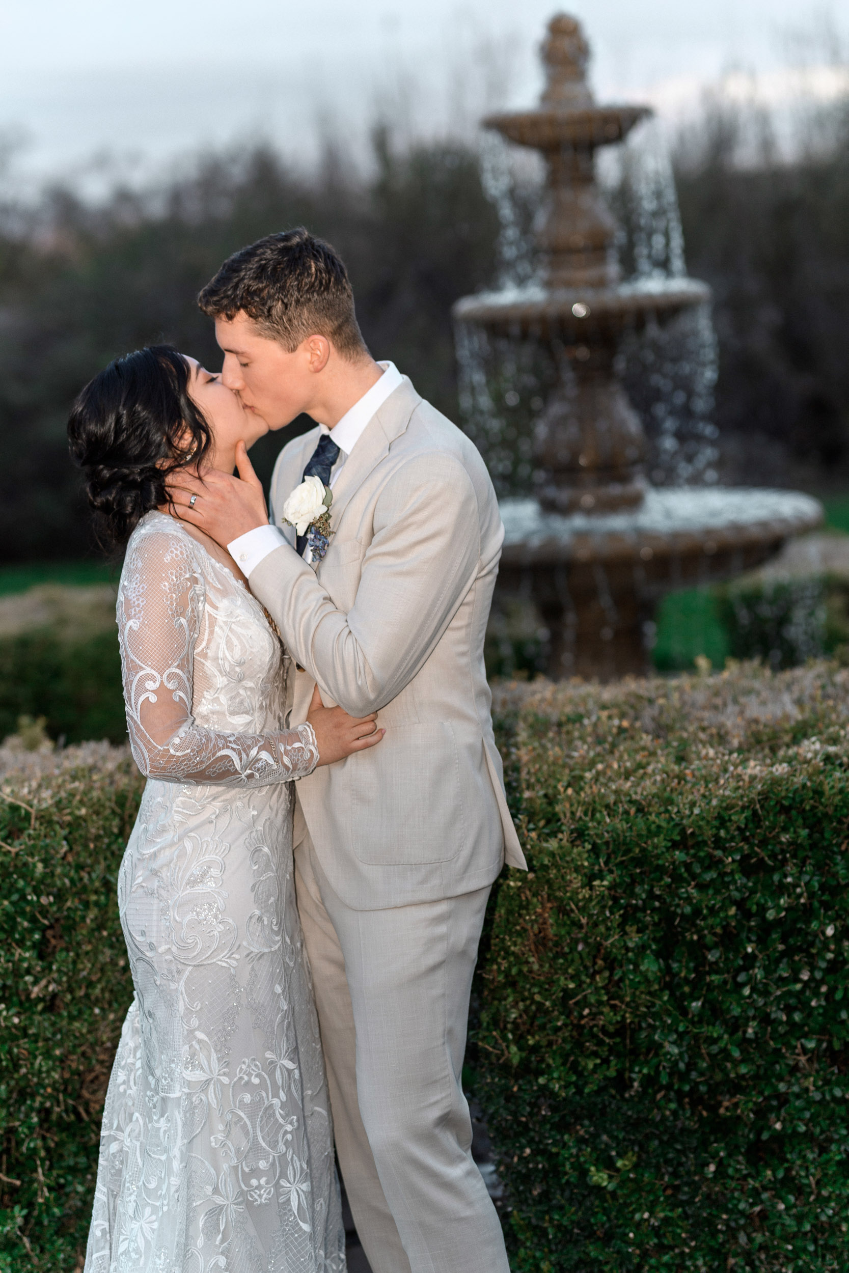 A bride and groom kiss in front of a fountain.