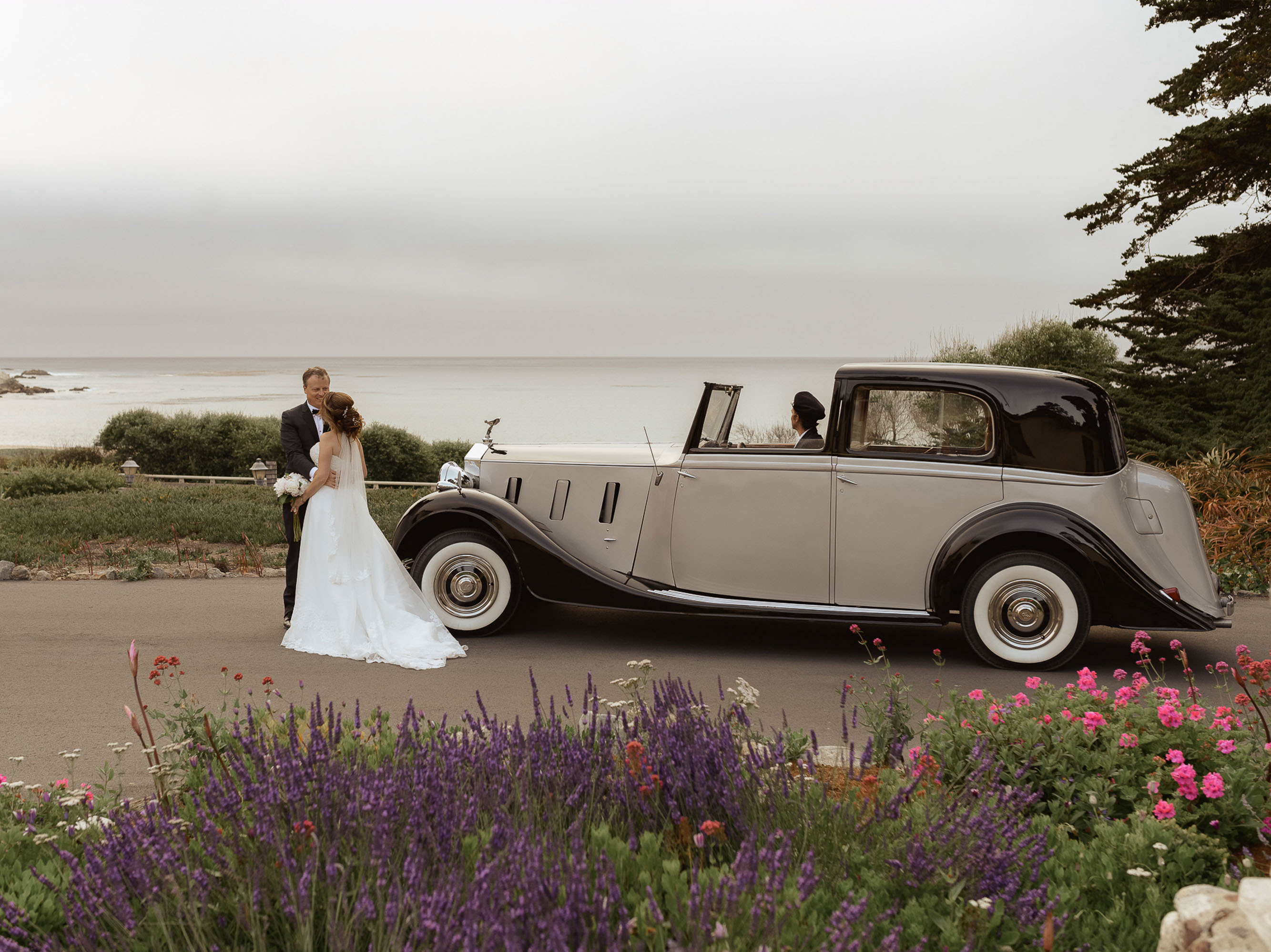 A bride and groom standing in front of a vintage car.