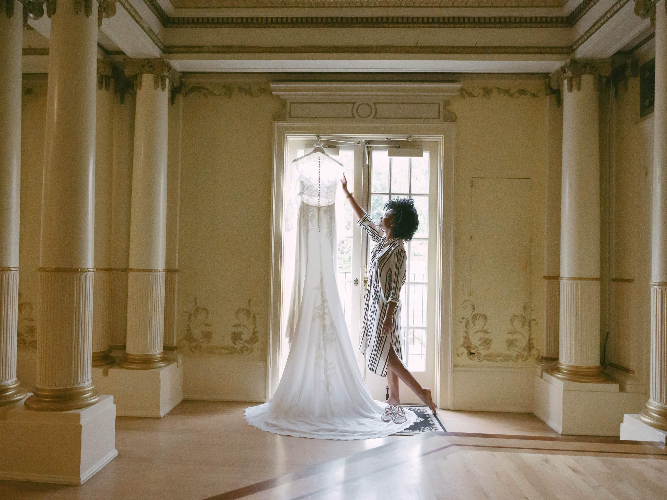 A bride is hanging her wedding dress in an ornate room.