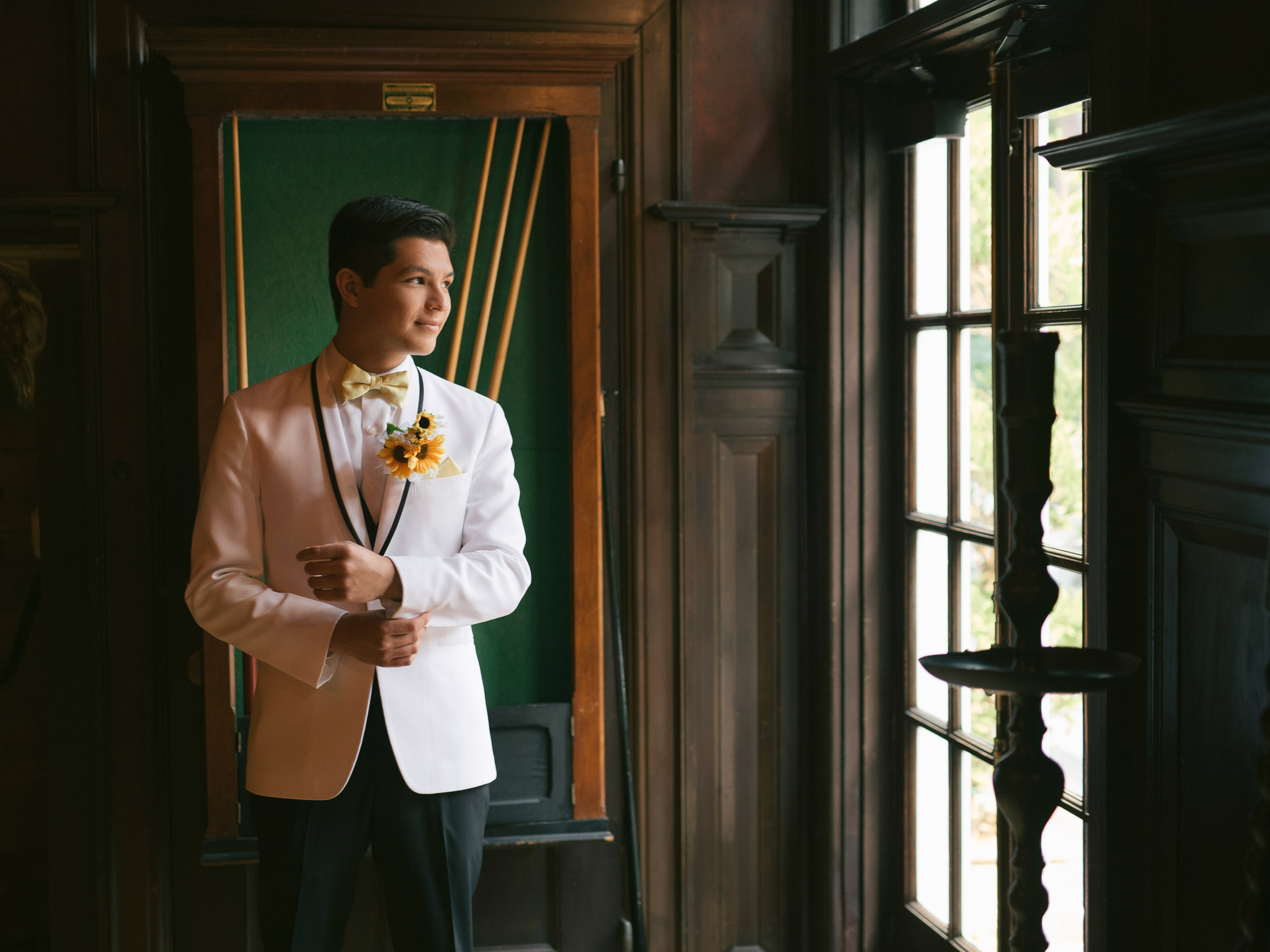 A groom in a white tuxedo standing in a doorway.