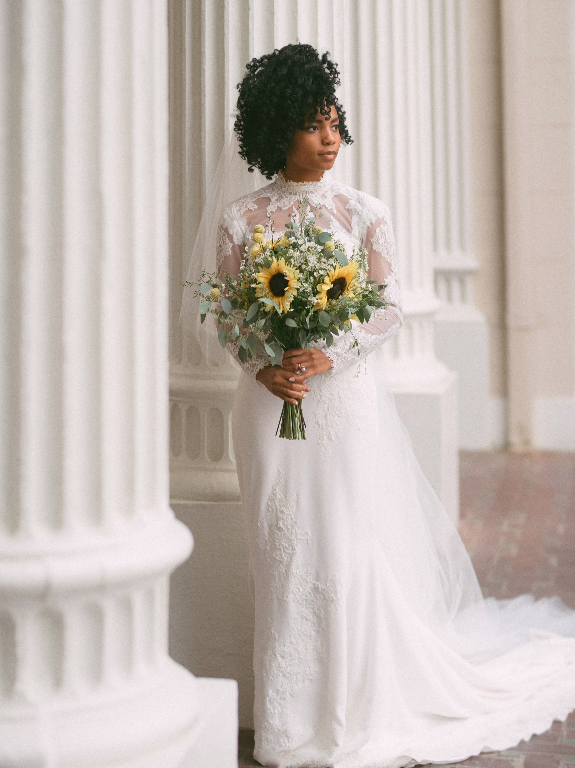 A bride with a bouquet of sunflowers in front of columns.